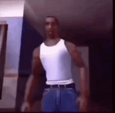 A Man Is Standing In A Room Wearing A White Tank Top And Blue Jeans . GIF