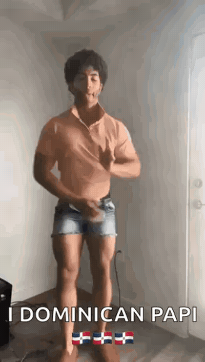 A Man Is Standing In A Room Wearing Shorts And A Shirt That Says Dominican Papi . GIF