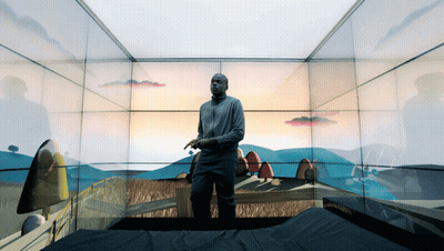 A Man Is Standing In A Room With A Painting Of A Landscape On The Wall GIF