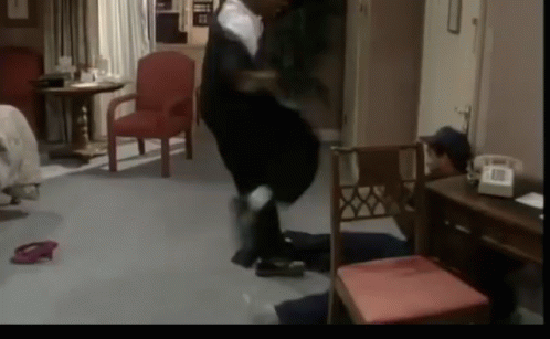 A Man Is Standing In A Room With A Red Chair GIF