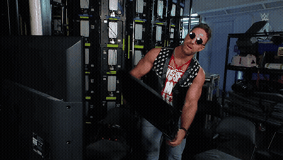 A Man Is Standing In A Room With A Wrestling Logo On The Wall GIF