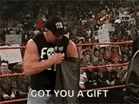 A Man Is Standing In A Wrestling Ring Holding A Black Shirt And Says `` Got You A Gift '' . GIF