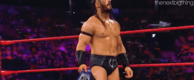 A Man Is Standing In A Wrestling Ring Holding A Championship Belt . GIF