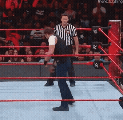 A Man Is Standing In A Wrestling Ring With A Referee In The Background . GIF