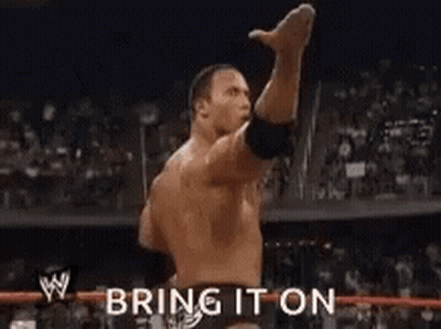 A Man Is Standing In A Wrestling Ring With His Arm In The Air And The Words `` Bring It On '' Behind Him . GIF