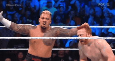 A Man Is Standing In A Wrestling Ring With His Arms Outstretched Next To Another Man . GIF