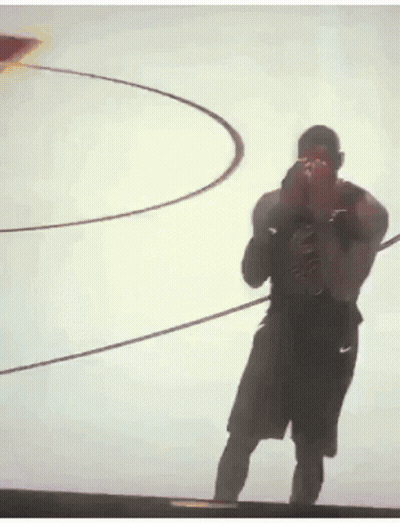 A Man Is Standing In Front Of A Basketball Hoop And Taking A Picture With His Phone . GIF