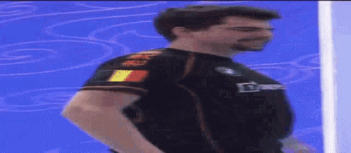 A Man Is Standing In Front Of A Blue Wall Wearing A Black Shirt That Says ' Bmw ' On It GIF