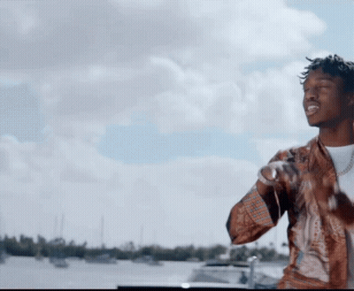 A Man Is Standing In Front Of A Body Of Water With Boats In The Background GIF