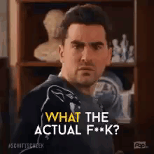 A Man Is Standing In Front Of A Bookshelf And Asking What The Actual F * Ck . GIF