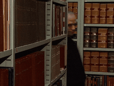 A Man Is Standing In Front Of A Bookshelf With A Book Titled ' A Brief History Of The World ' On It GIF