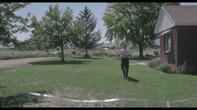 A Man Is Standing In Front Of A Brick House Holding A Piece Of Paper GIF
