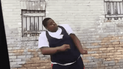 A Man Is Standing In Front Of A Brick Wall Dancing . GIF