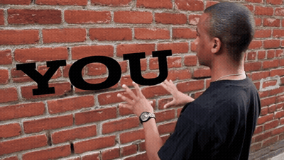 a man is standing in front of a brick wall that has the word you written on it