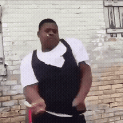 A Man Is Standing In Front Of A Brick Wall Wearing Sunglasses And A Vest . GIF