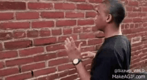 A Man Is Standing In Front Of A Brick Wall With His Hands Outstretched . GIF