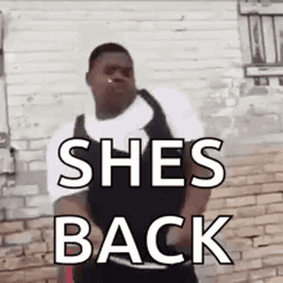 A Man Is Standing In Front Of A Brick Wall With The Words `` She 'S Back '' Written On His Chest . GIF