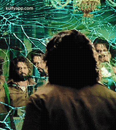 A Man Is Standing In Front Of A Broken Mirror With A Group Of People Behind Him . GIF