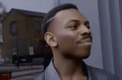 A Man Is Standing In Front Of A Building Looking At The Camera . GIF