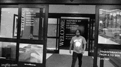 A Man Is Standing In Front Of A Building With A Welcome Sign On It . GIF