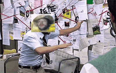 A Man Is Standing In Front Of A Bulletin Board With A Picture Of A Man In A Cowboy Hat On It . GIF