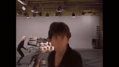 A Man Is Standing In Front Of A Camera In A Studio With A Drum Set In The Background . GIF