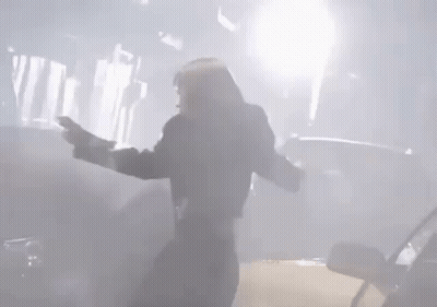 A Man Is Standing In Front Of A Car With His Arms Outstretched In A Foggy Room . GIF