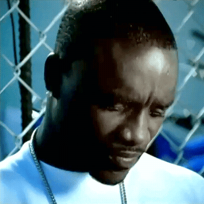 A Man Is Standing In Front Of A Chain Link Fence And Looking Down . GIF