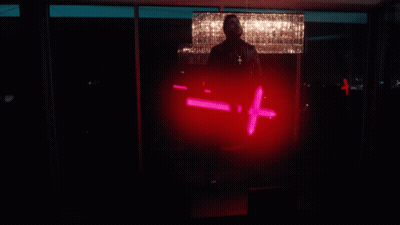 A Man Is Standing In Front Of A Chandelier And Holding A Red Light That Says - = + GIF