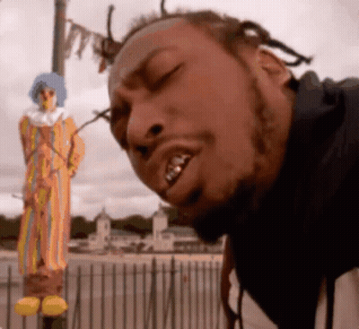 A Man Is Standing In Front Of A Clown Statue With His Eyes Closed GIF