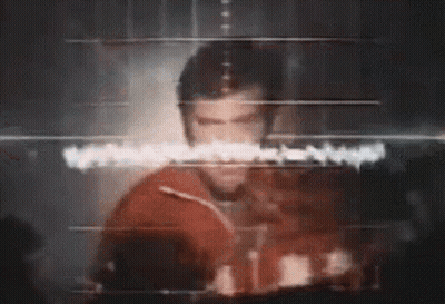 A Man Is Standing In Front Of A Computer Screen With A Heartbeat Monitor . GIF