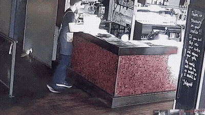 A Man Is Standing In Front Of A Counter In A Restaurant With A Sign On The Wall That Says Family On Your Shoulder GIF