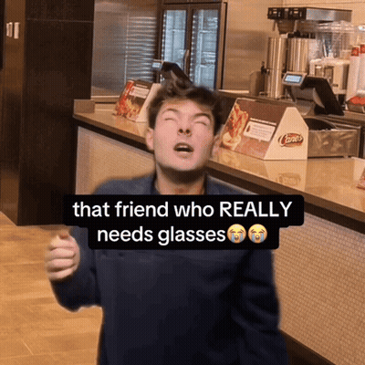 A Man Is Standing In Front Of A Counter With A Sign That Says " That Friend Who Really Needs Glasses " GIF