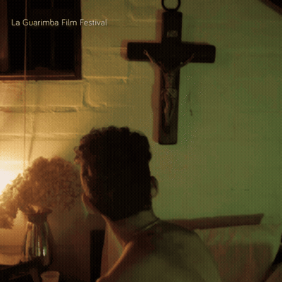 A Man Is Standing In Front Of A Cross With La Guarimba Film Festival Written Above Him GIF