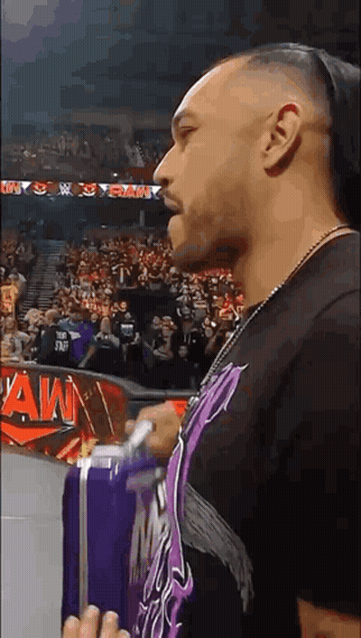 A Man Is Standing In Front Of A Crowd In A Stadium Holding A Purple Suitcase . GIF