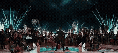 A Man Is Standing In Front Of A Crowd Of People At A Party With Fireworks Going Off In The Background . GIF