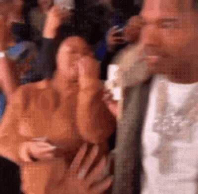 A Man Is Standing In Front Of A Crowd Of People Holding A Cell Phone . GIF