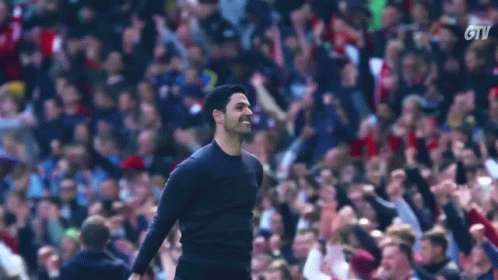 A Man Is Standing In Front Of A Crowd Of People In A Stadium And Raising His Fist In The Air . GIF