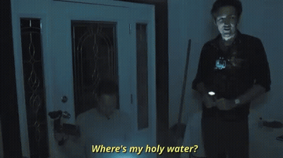 A Man Is Standing In Front Of A Door Holding A Flashlight And Asking Where Is My Holy Water . GIF