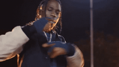 A Man Is Standing In Front Of A Fire At Night Holding A Box In His Hand . GIF