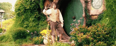 A Man Is Standing In Front Of A Green Door In A Garden Holding A Sword . GIF