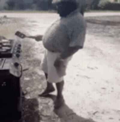 A Man Is Standing In Front Of A Grill Holding A Spatula And A Spoon . GIF
