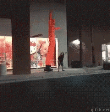 A Man Is Standing In Front Of A Hello Kitty Sign And A Red Air Dancer GIF