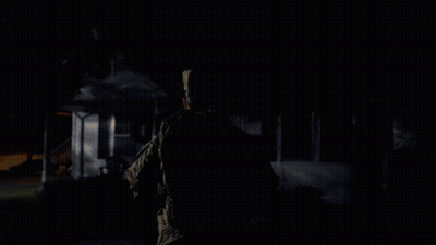A Man Is Standing In Front Of A House That Has Christmas Lights On It GIF