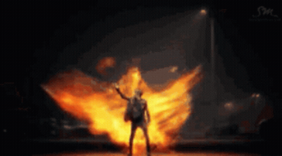 A Man Is Standing In Front Of A Huge Explosion Of Fire . GIF