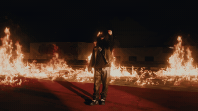 A Man Is Standing In Front Of A Large Amount Of Flames GIF