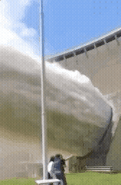 A Man Is Standing In Front Of A Large Building With A Hose Spraying Water . GIF