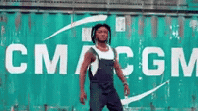 A Man Is Standing In Front Of A Large Green Container That Says Cmcgm GIF