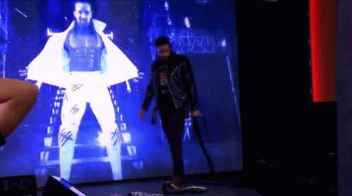 A Man Is Standing In Front Of A Large Screen That Says Wwe GIF