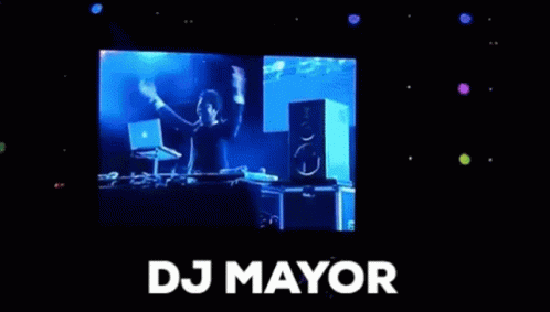 A Man Is Standing In Front Of A Large Screen With The Word Dj Mayor On It . GIF